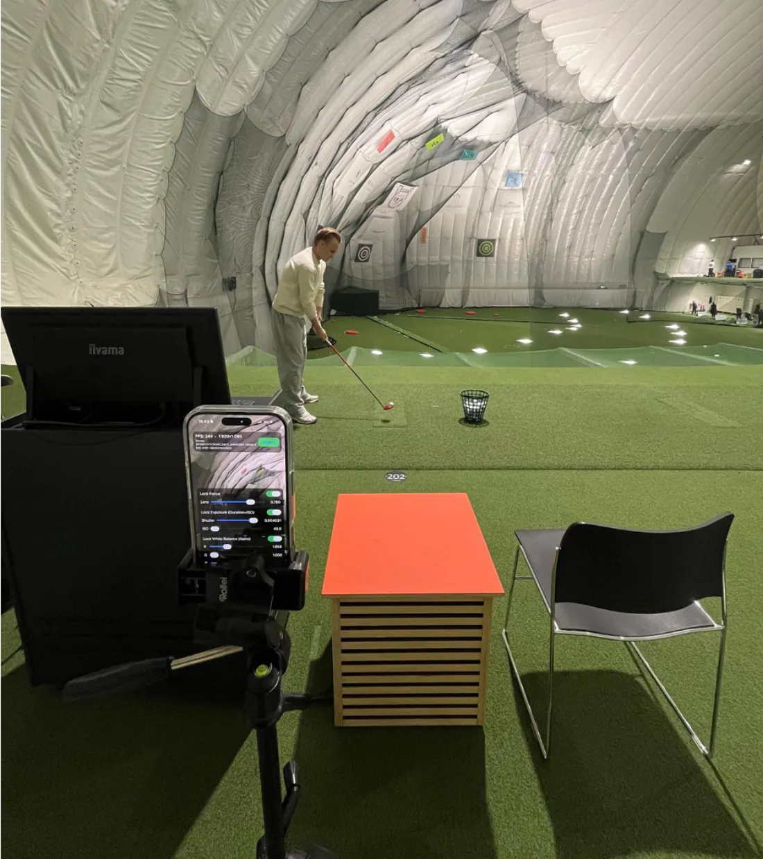 Golfer practicing with phone camera setup at indoor range